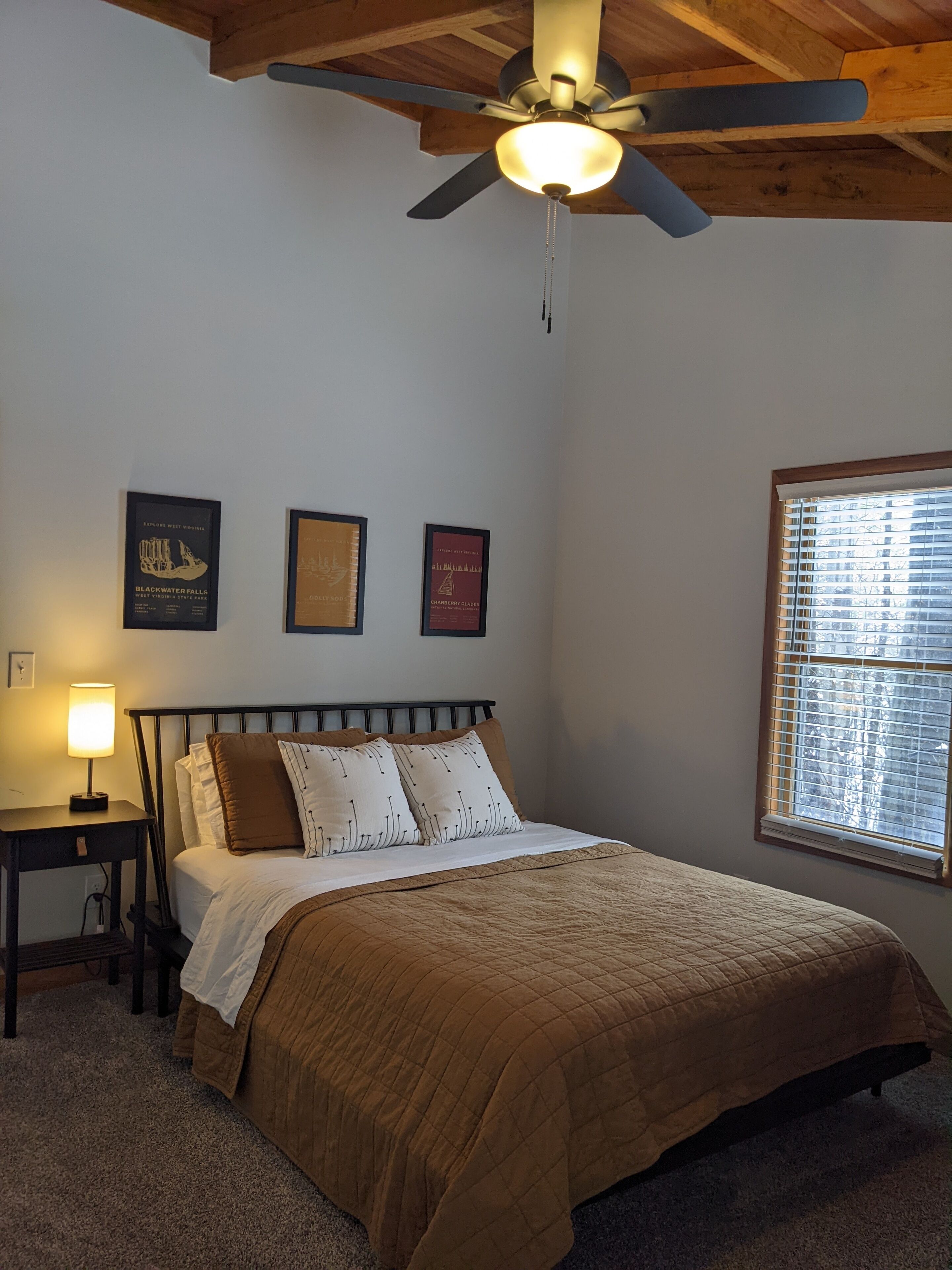 A bedroom with a bed, a nightstand, a ceiling fan, and three framed pictures on the wall.