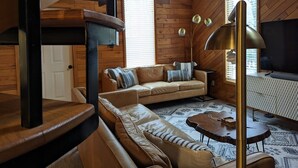 A cozy living room with a sofa, a coffee table, and a TV. There is a staircase with a wooden railing and a window with blinds. - Access to everything yet secluded and chic, this hideaway has it all. (Davis)