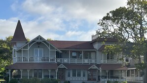 Una casa grande de dos pisos con una torre destacada, varios balcones y un césped bien cuidado.