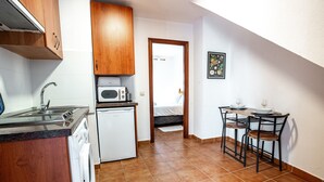 A compact kitchen with a washing machine, a microwave, and a small refrigerator. There is a dining area with two chairs and a table. - Marbella Village  | Studio with Juliette Balcony (Marbella)