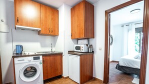 A compact kitchen with wooden cabinets, a washing machine, a microwave, and a small countertop. - Marbella Village  | Studio with Juliette Balcony (Marbella)