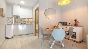 A modern kitchen with white cabinets, a dining table with chairs, and a hanging light fixture.