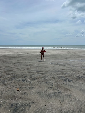 A person standing on a sandy beach with the ocean in the background.