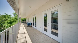 Ein überdachter Balkon mit weißer Reling, einem blauen Stuhl und einer Glastür, die auf eine Terrasse führt.