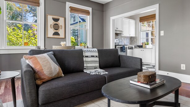 Een moderne woonkamer met een donkergrijze bank, een ronde salontafel en uitzicht op de keuken door een open doorgang.