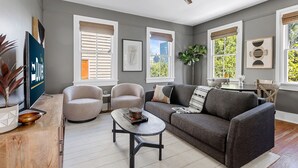 Een moderne woonkamer met een grijze bank, twee fauteuils, een salontafel en een plafondventilator.
