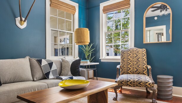 A living room with a sofa, a patterned armchair, a wooden coffee table, and a large mirror on the wall. - Steps Away from Historic King! | The Sutton - B (Charleston)