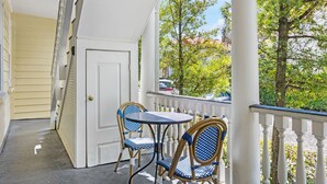 A porch with a white railing, a door, and two wicker chairs with blue cushions. - Steps Away from Historic King! | The Sutton - B (Charleston)