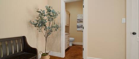 A hallway with a dark wooden bench, a potted plant, a white door, and a bathroom visible in the background.