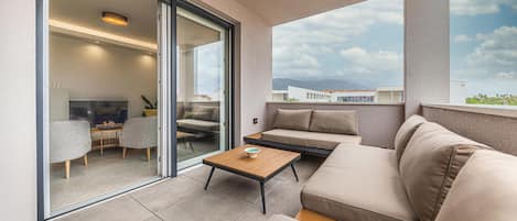 A modern balcony with a sofa, a small table, and a glass door leading to an interior space with a dining area.
