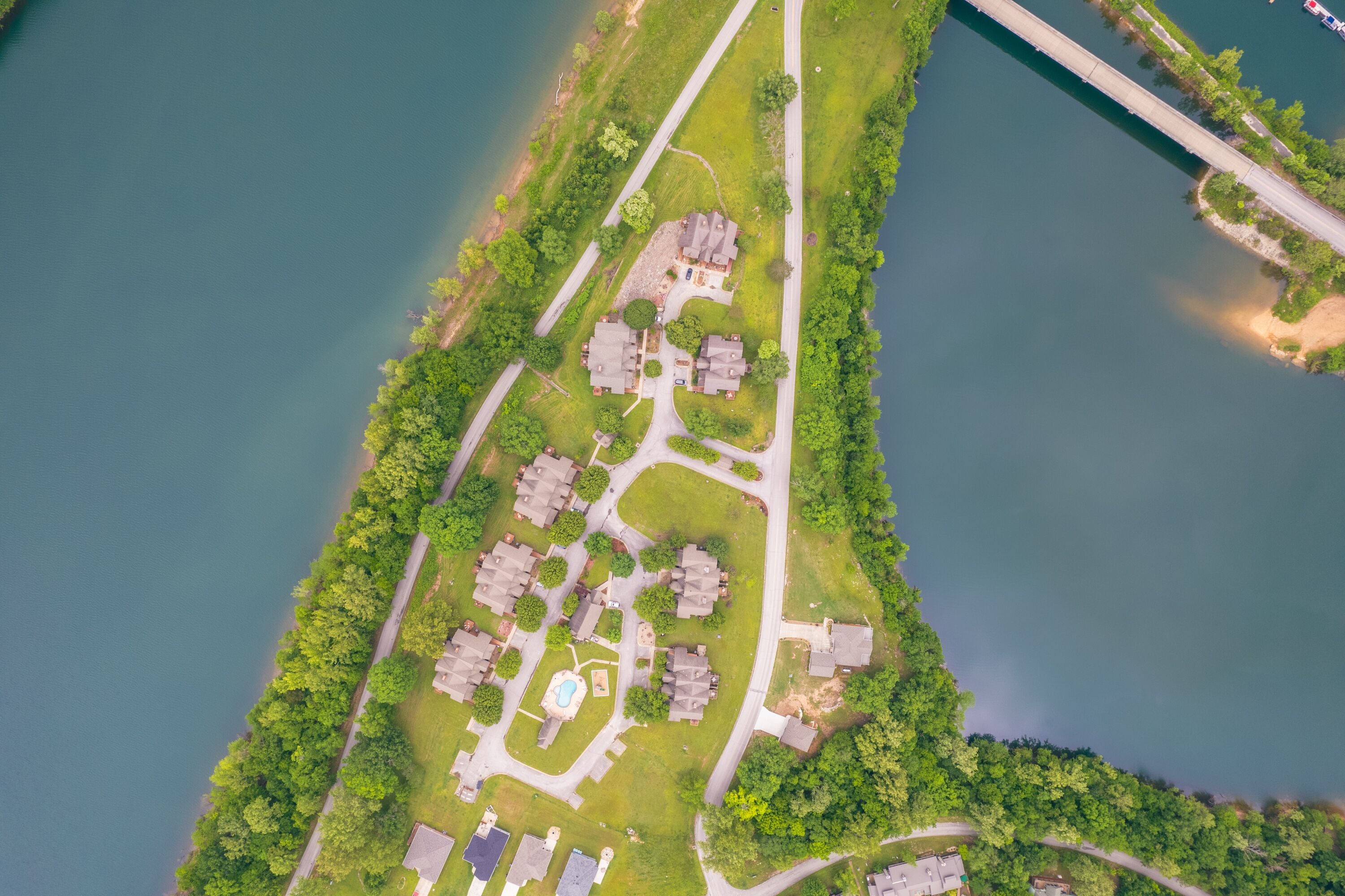 An aerial view of a residential area with houses, a swimming pool, and a bridge.