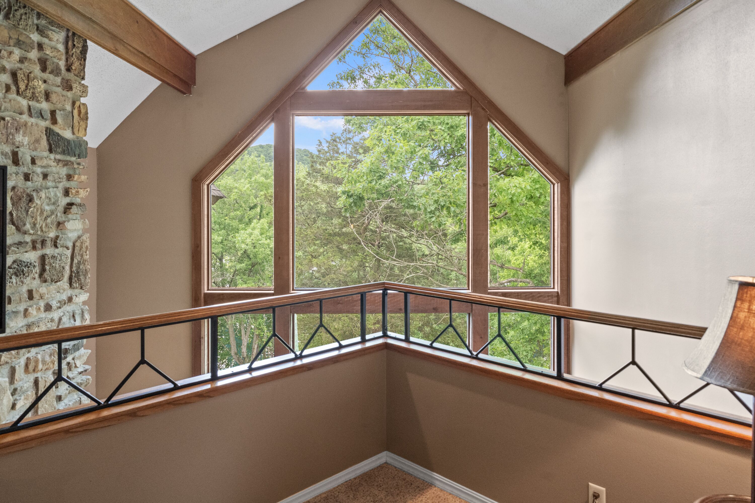 A corner room with a large window, stone wall, and a wooden railing.