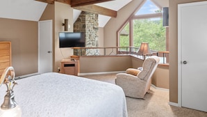 A bedroom with a large bed, a stone fireplace, a TV mounted on the wall, and a view of the outdoors through a window. - Table Rock Landing Resort (Eureka Springs)