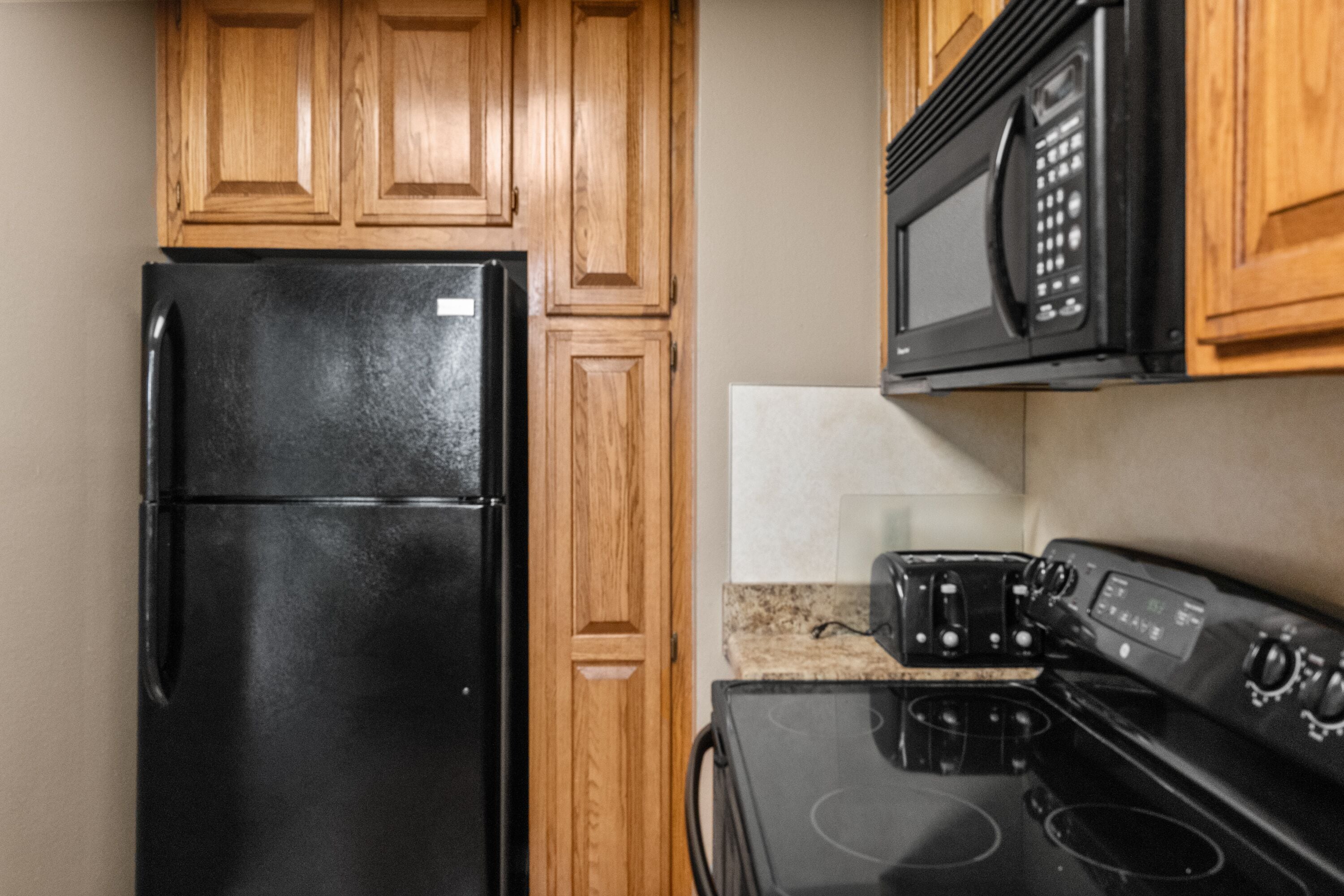 A kitchen with wooden cabinets, a black refrigerator, a microwave, and a stove.
