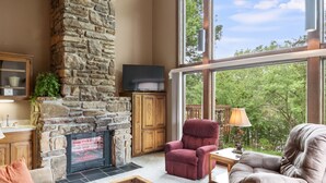 A living room with a stone fireplace, large windows, and comfortable seating. - Table Rock Landing Resort (Eureka Springs)