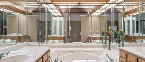 Ein modernes Badezimmer mit großem Spiegel, zwei Waschbecken, einer Badewanne, Holzschränken und einer Marmorarbeitsplatte.