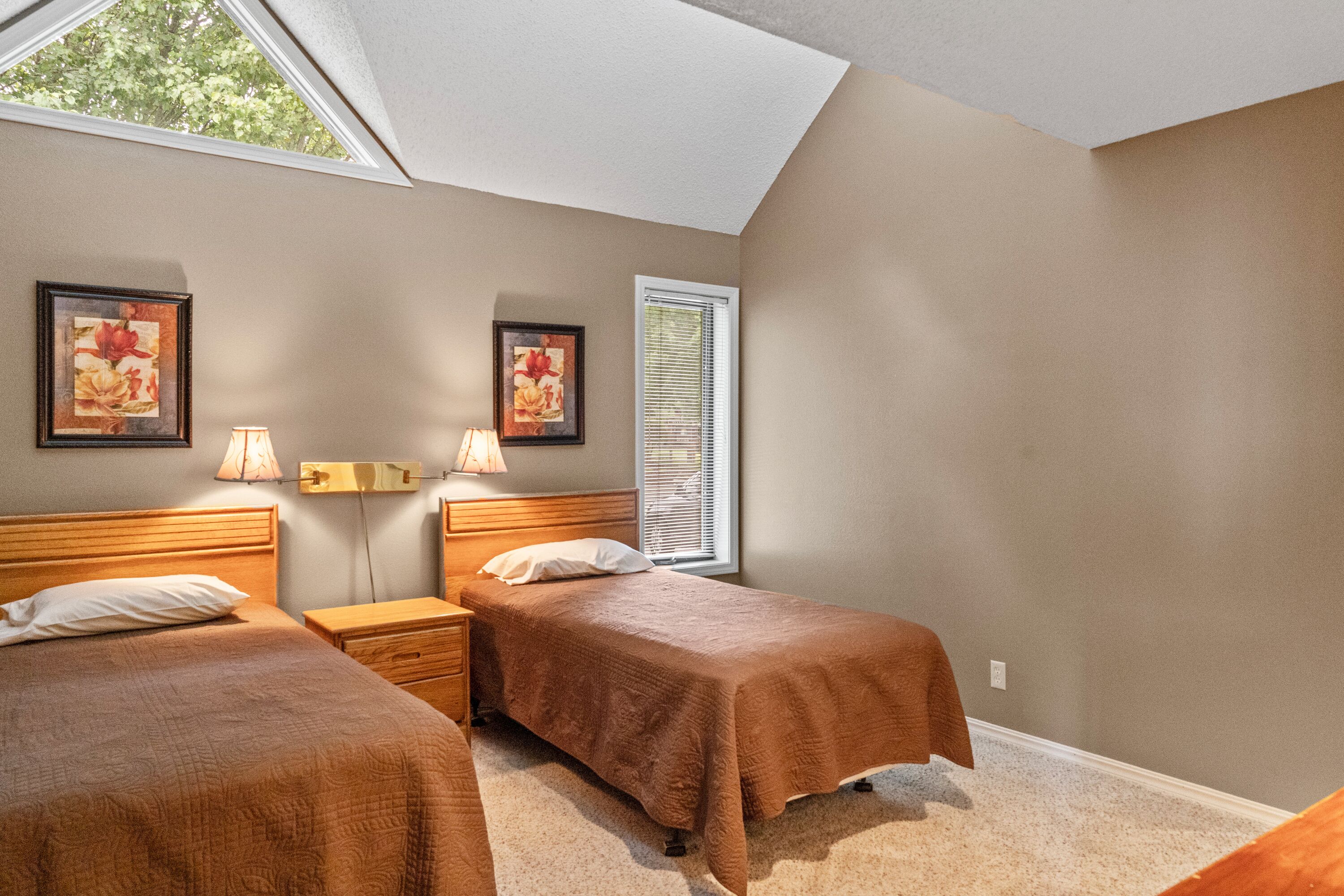 A bedroom with two beds, a skylight, and two wall-mounted lamps.