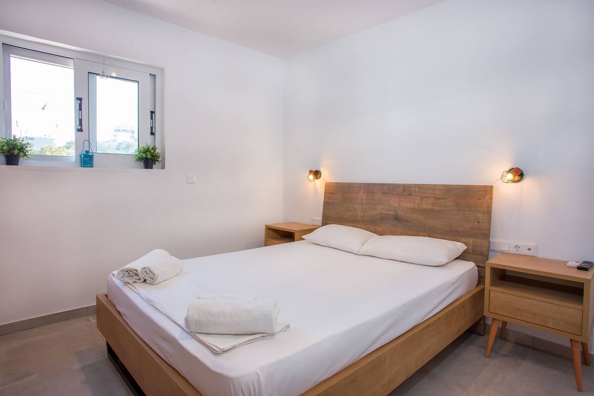 Una cama bien hecha con sábanas blancas, un cabecero de madera y dos mesitas de noche con lámparas.