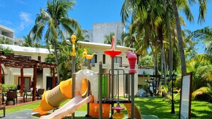 Ein Spielplatz mit Rutschen und Klettergerüsten, umgeben von Palmen und einem Gebäude mit Balkon.