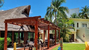 Ein Resort mit Sitzgelegenheiten unter einem Reetdach, einem Poolbereich und Palmen.