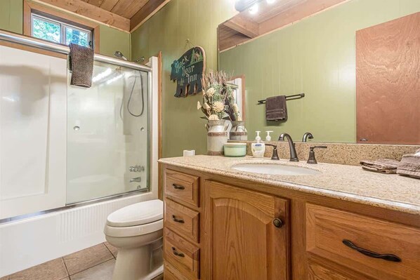 Un baño con cabina de ducha de vidrio, inodoro, armarios de madera, lavamanos con espejo y un cartel sobre el lavamanos.