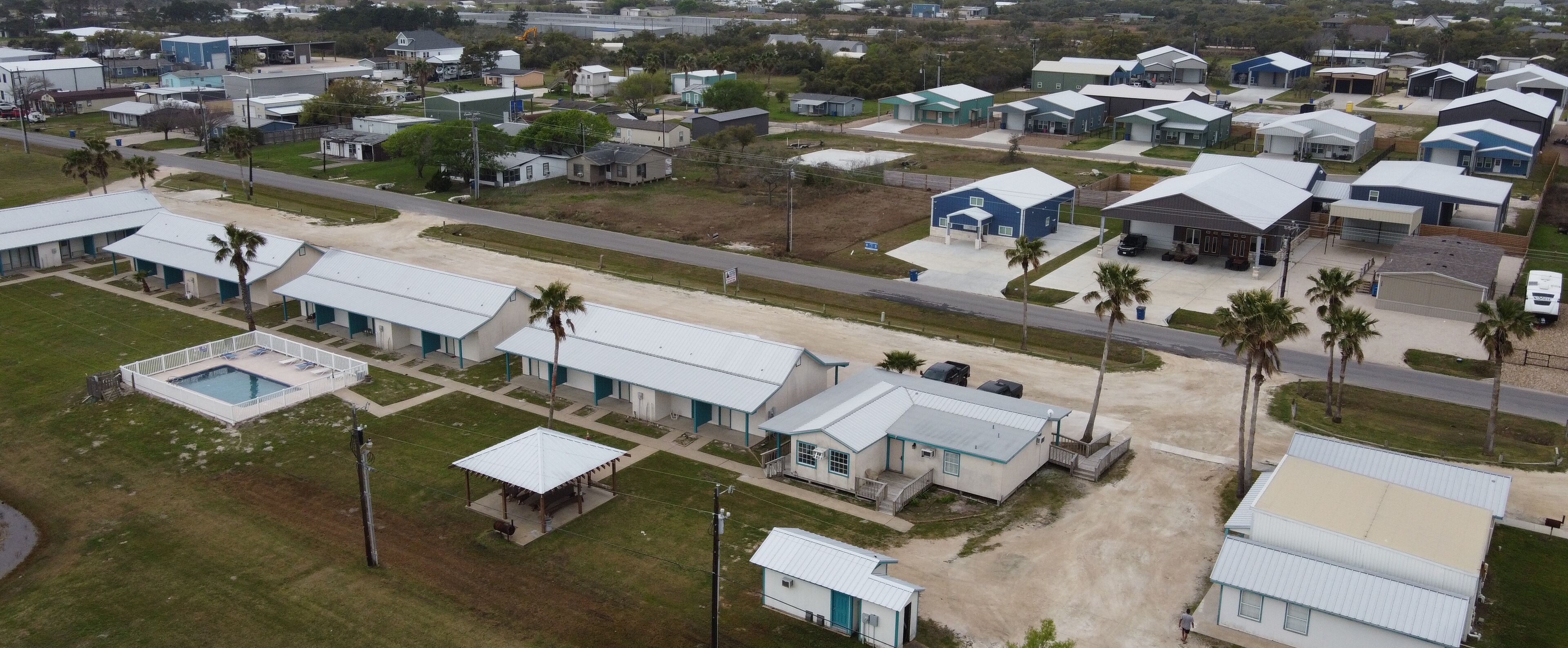An aerial view of a residential area with multiple single-story houses, a swimming pool, and a few palm trees.