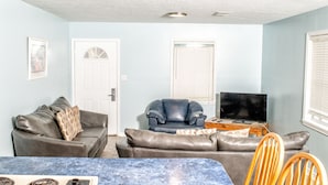 A living room with a sofa, a chair, a TV, and a dining area with a table and chairs. - Captain Quarters Motel (Port O Connor)