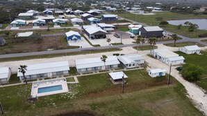 An aerial view of a campground with multiple cabins, a swimming pool, and a large body of water. - Captain Quarters Motel (Port O Connor)