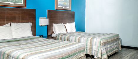 A hotel room with two beds, a nightstand, a lamp, and two framed pictures on the wall.