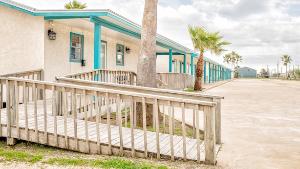 A motel with a wooden deck and a palm tree. - Captain Quarters Motel (Port O Connor)