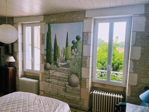 Un dormitorio con un mural de un jardín, un radiador, una cama y una ventana con vistas a la vegetación.