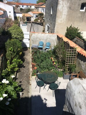 Un patio con una mesa redonda y sillas, rodeado de plantas en macetas y un muro de piedra.