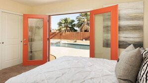 Een slaapkamer met een bed, een witte deur en uitzicht op een zwembad en palmbomen.