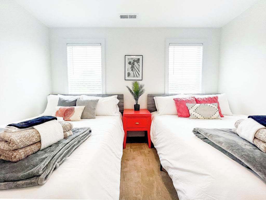 Une chambre avec deux lits, une table de chevet rouge et un tableau encadré accroché au mur.