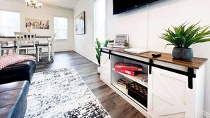 Una sala de estar moderna con un televisor montado en la pared, una mesa de centro de madera, un sofá negro y un comedor al fondo.