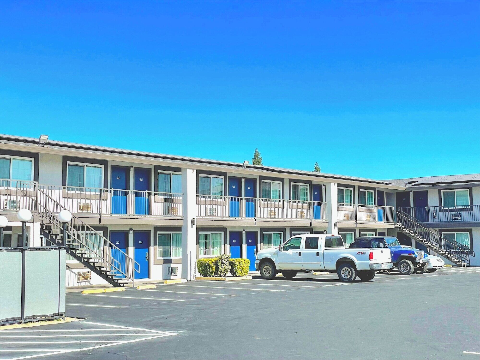 Un motel à plusieurs étages, doté de balcons et d’un parking où sont garés deux camions.