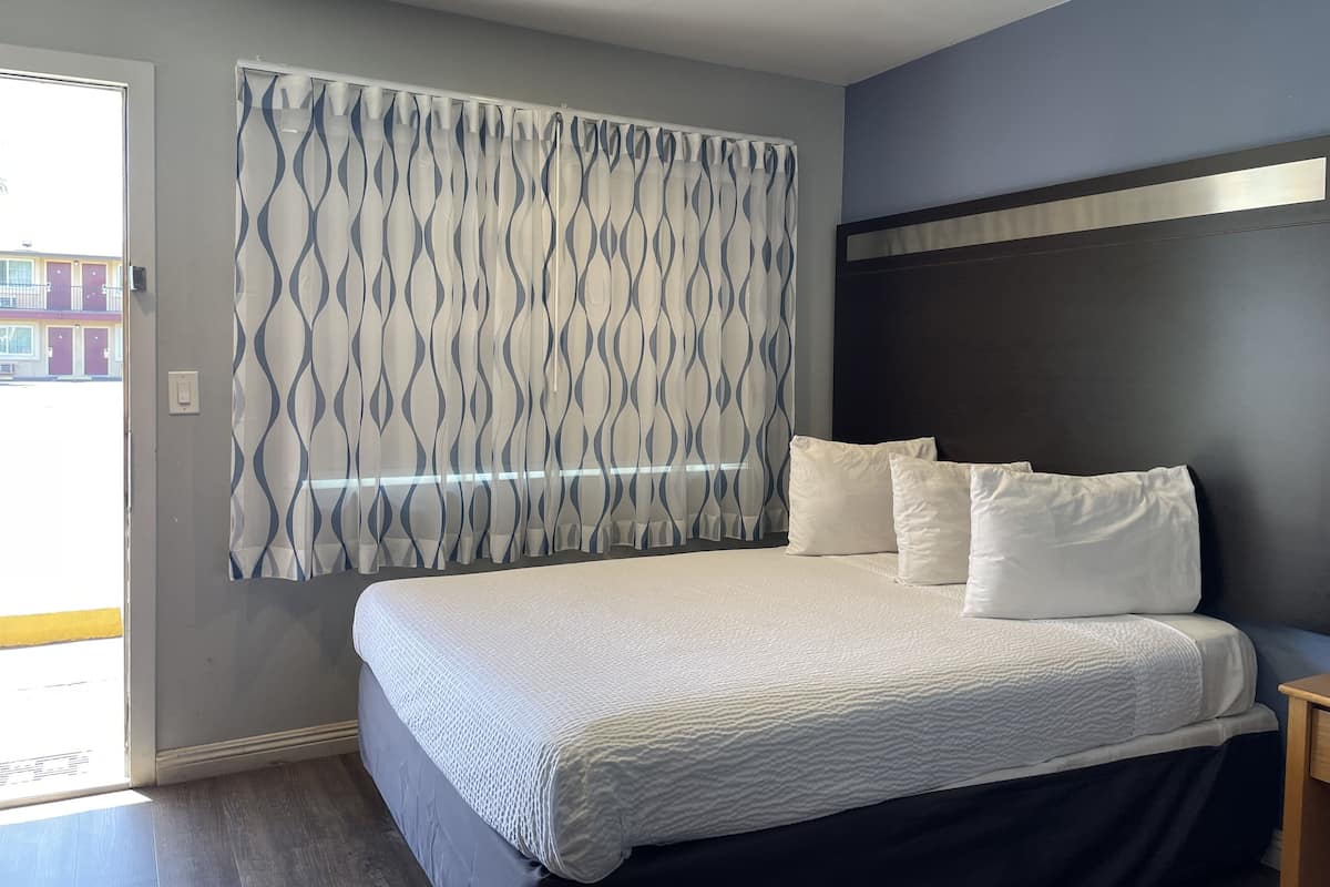 A bedroom with a bed, a headboard, and a window with patterned curtains.