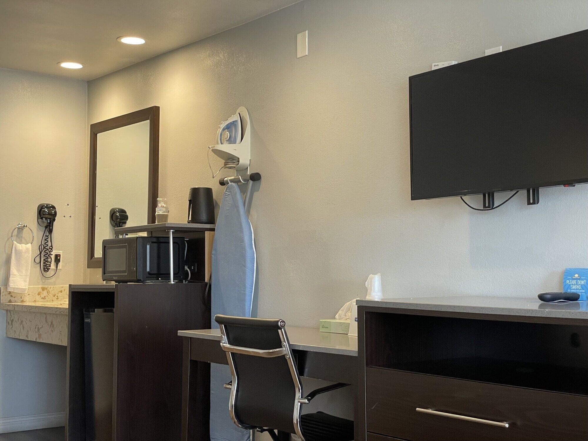 Habitación de hotel con escritorio, silla, microondas, cafetera y televisor montado en la pared.