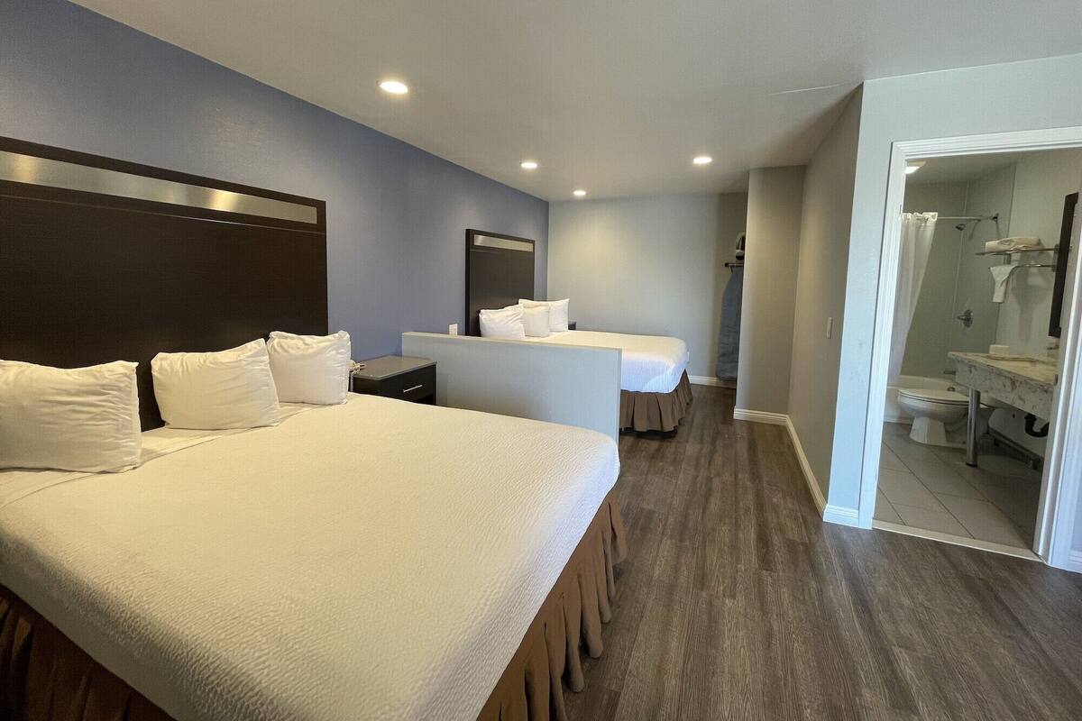 A hotel room with two beds, a bathroom, and a shower area.