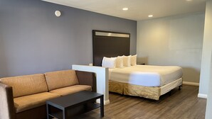 A hotel room with a brown sofa, a small table, a bed with white bedding, and a dark headboard. - Motel 6 Yuba City, CA (Yuba City)