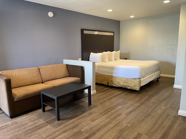 A hotel room with a brown sofa, a small table, a bed with white bedding, and a dark headboard.