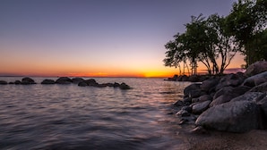 A beach with calm waters, large rocks, and trees at sunset. - Quiet Northwoods Cabin on Leech Lake, Minnesota (Federal Dam)