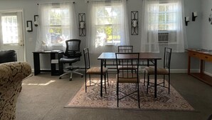 Un área de comedor con una mesa, sillas y un tapete. Hay ventanas con cortinas, un ventilador de techo y una puerta.