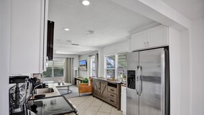 Una cocina moderna con refrigerador de acero inoxidable, encimeras de granito y un amplio ventanal con vistas al exterior.