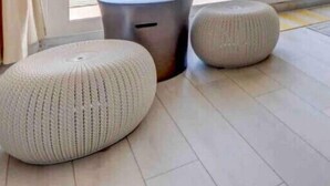 A modern room with a large window overlooking a balcony with a railing. There are two round ottomans and a small round table on the floor. - The Lazy Place: Gulf Penthouse, High Ceiling &Bunk (Panama City Beach)