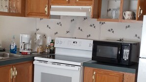 A kitchen with wooden cabinets, a white stove, a microwave, and a tiled backsplash. - The 100 Acre Woods located in the Appalachian mountains Clintwood Va (Clintwood)