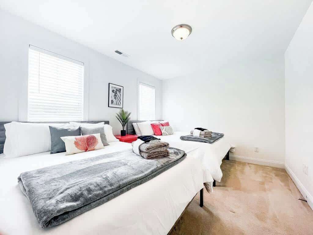 Une chambre moderne avec deux lits, des murs blancs et un luminaire au plafond.