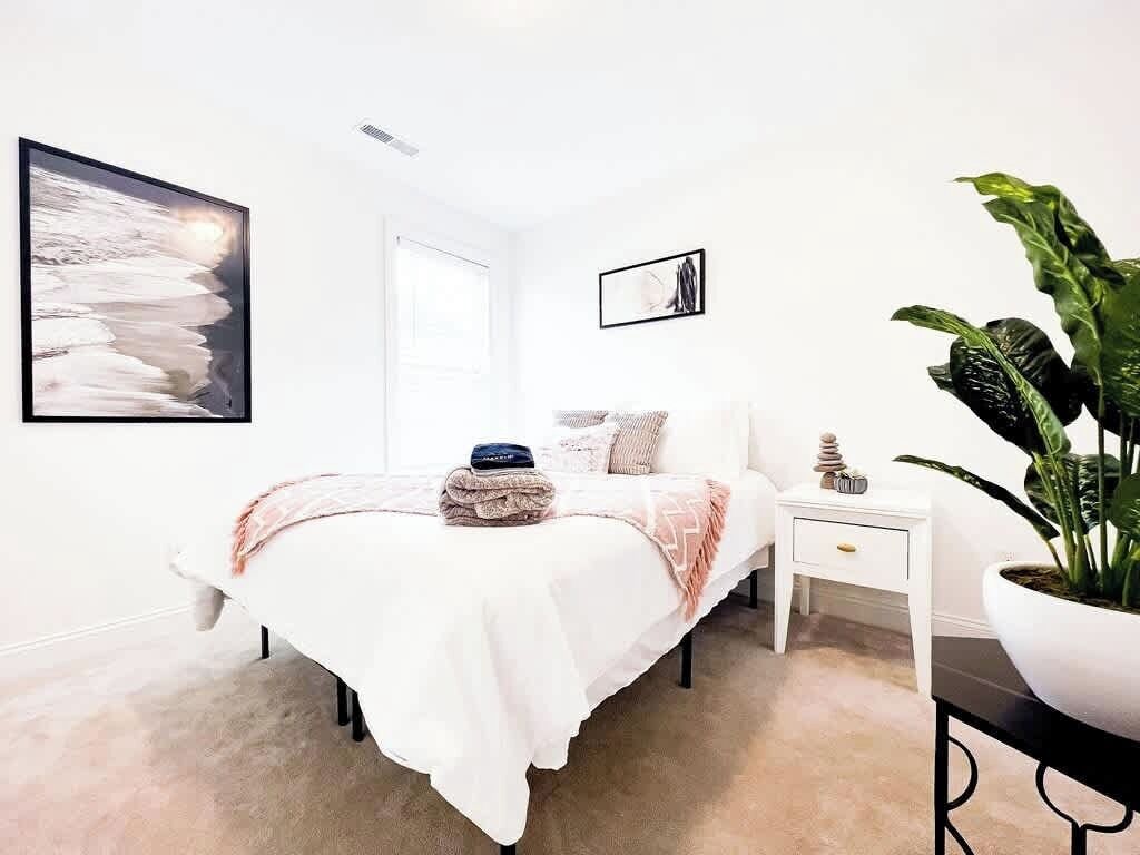 Une chambre à coucher moderne avec un lit, une table de chevet et une grande plante en pot.