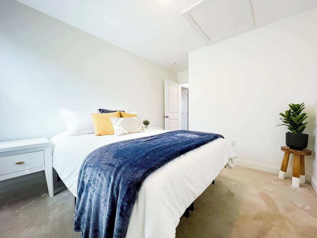 Een slaapkamer met een bed, nachtkastje en een bloempot.