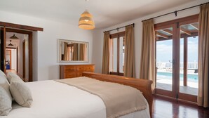 Un dormitorio amplio con una cama grande, cabecera de madera, un espejo sobre el tocador y vistas a un balcón con piscina.